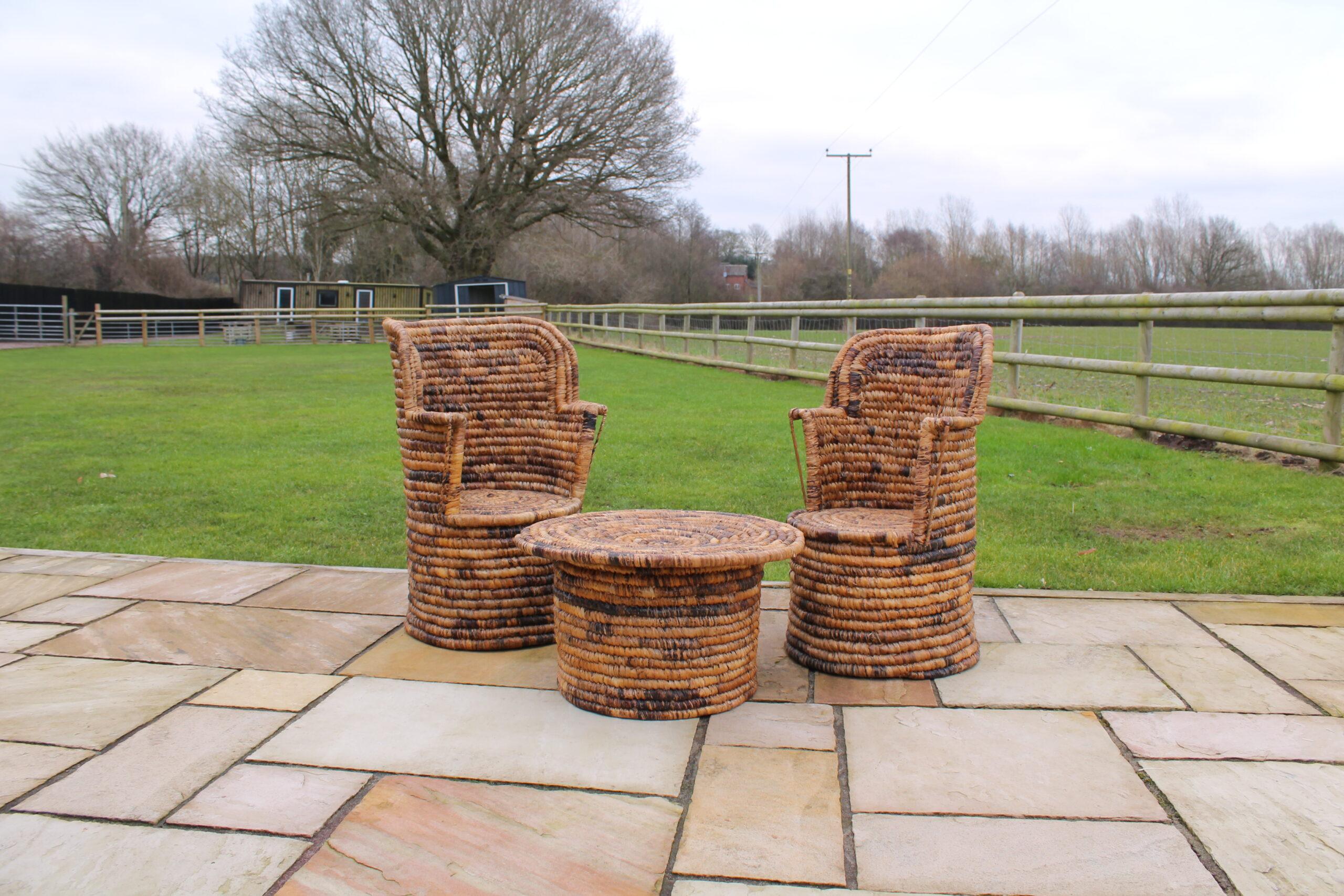 Two handmade African woven high-back chairs with round table on a stone patio in an English countryside garden