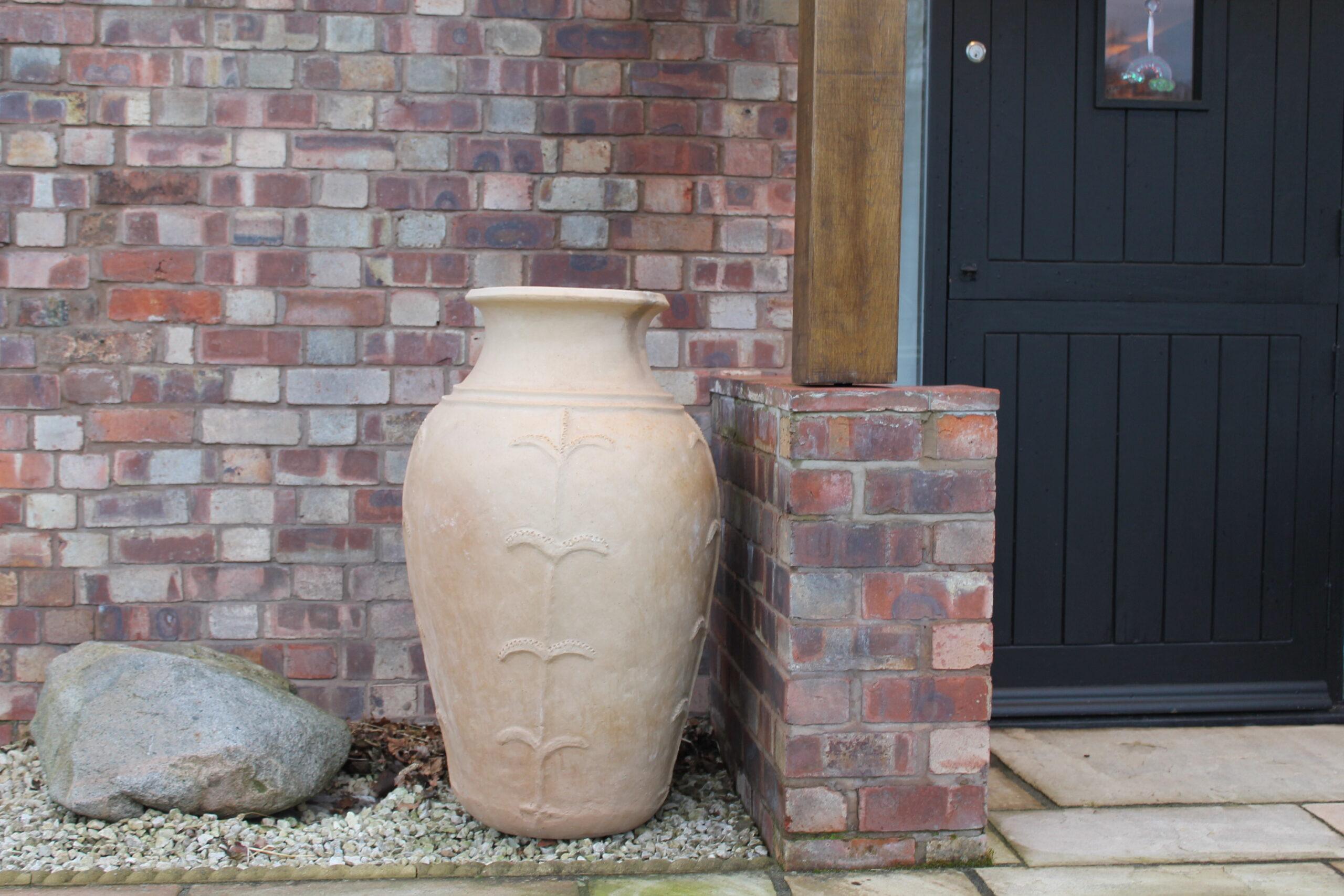 Large handcrafted African clay vase placed outside a British brick house beside a black door, demonstrating outdoor use